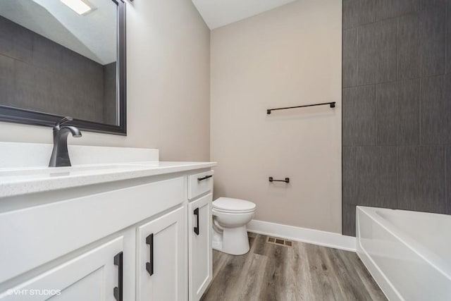 bathroom featuring vanity, toilet, baseboards, wood finished floors, and visible vents