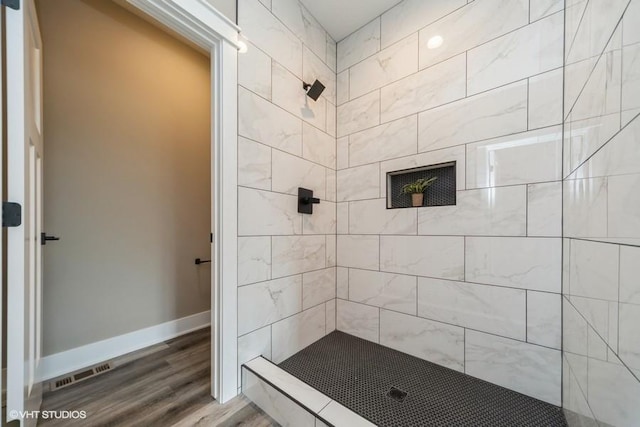 full bath featuring baseboards, a tile shower, wood finished floors, and visible vents