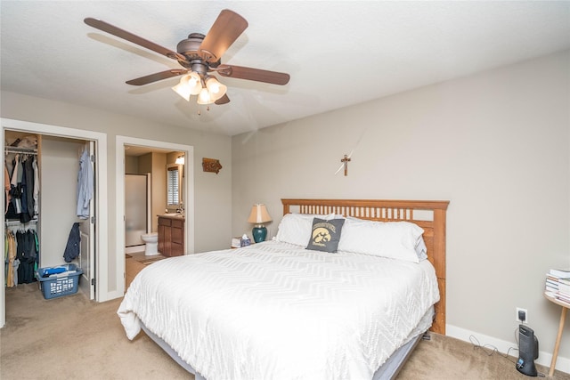 bedroom with a closet, light carpet, a walk in closet, a ceiling fan, and ensuite bath