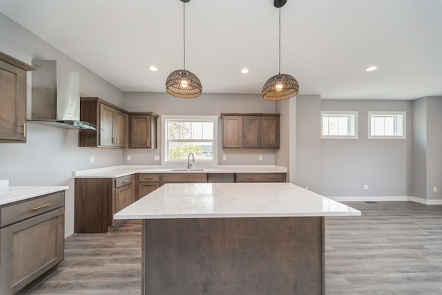 kitchen featuring recessed lighting, wall chimney exhaust hood, light stone counters, a sink, and light wood-style flooring