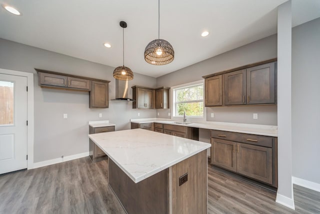 kitchen with wood finished floors, baseboards, a center island, wall chimney exhaust hood, and a sink