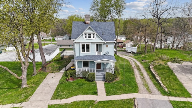 victorian home with a front lawn, roof with shingles, a chimney, a porch, and driveway