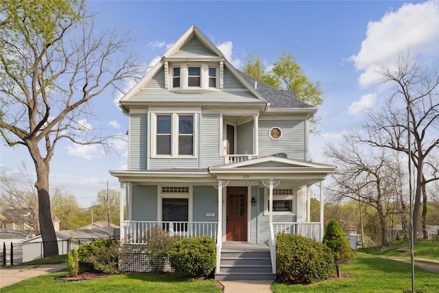 victorian home with a porch, fence, a shingled roof, and a front yard