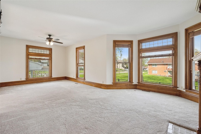 carpeted empty room with visible vents, a ceiling fan, baseboards, and a healthy amount of sunlight