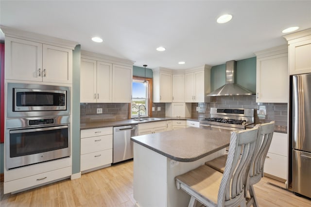 kitchen with a sink, light wood-style flooring, wall chimney range hood, and stainless steel appliances