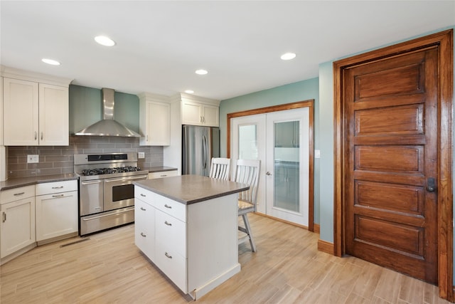 kitchen featuring wall chimney range hood, a breakfast bar area, appliances with stainless steel finishes, dark countertops, and light wood-style floors