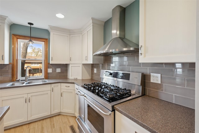 kitchen featuring wall chimney range hood, backsplash, decorative light fixtures, gas stove, and a sink