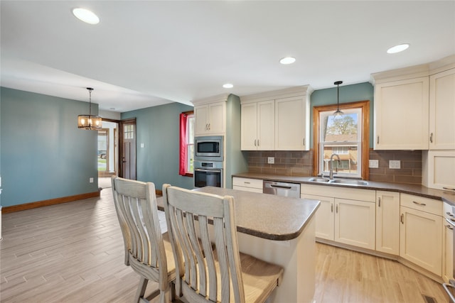 kitchen featuring a sink, light wood finished floors, stainless steel appliances, baseboards, and backsplash