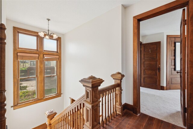 218 E Howard St, Colfax, IA 50054 - corridor with baseboards, dark wood-style flooring, a notable chandelier, and an upstairs landing