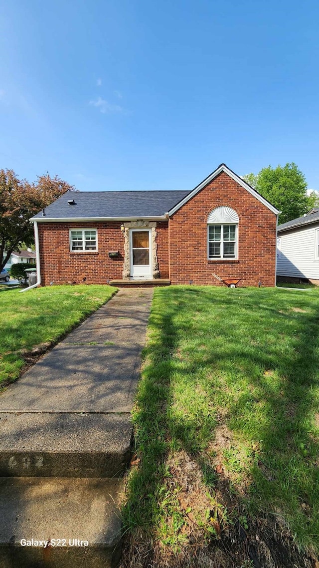 single story home featuring roof with shingles, a front lawn, and brick siding