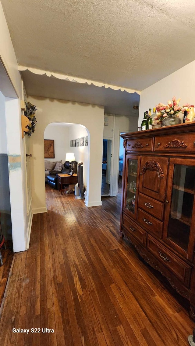 interior space with arched walkways, baseboards, dark wood-style flooring, and a textured ceiling