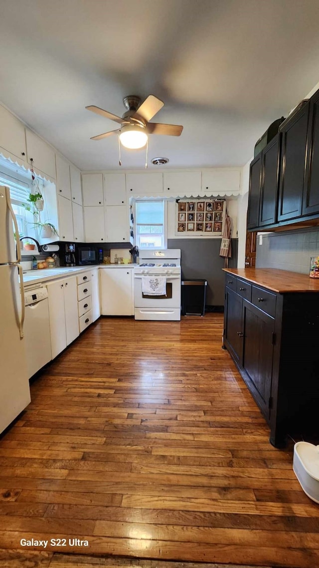 kitchen featuring visible vents, white appliances, ceiling fan, dark cabinets, and dark wood finished floors