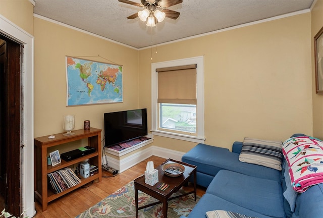 living area featuring ornamental molding, baseboards, a textured ceiling, a ceiling fan, and light wood finished floors
