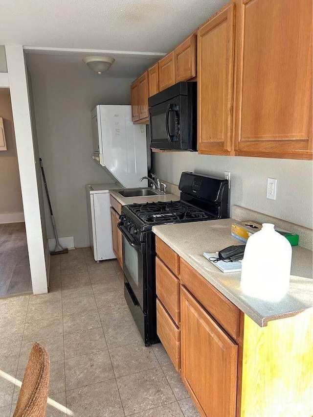 kitchen featuring brown cabinetry, light countertops, a sink, light tile patterned floors, and black appliances