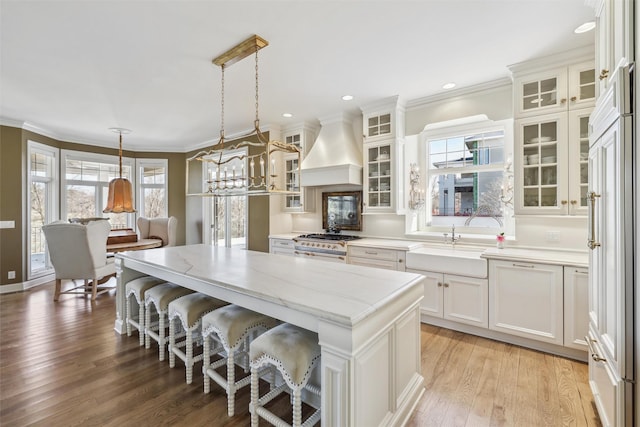 kitchen featuring light stone counters, a sink, a center island, custom exhaust hood, and range with gas cooktop