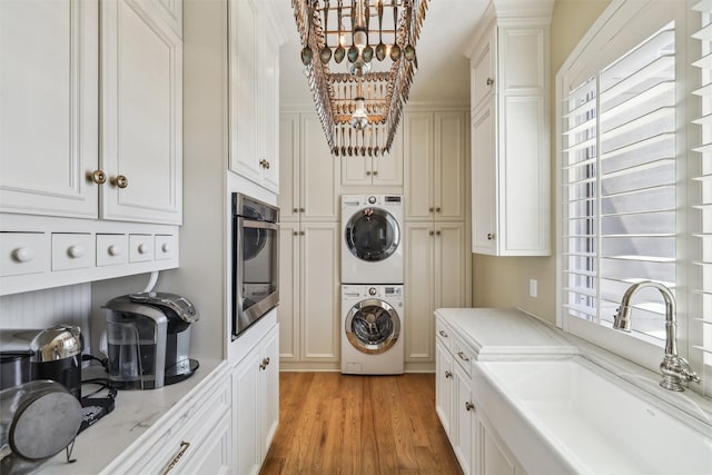 laundry area featuring a sink, a chandelier, a healthy amount of sunlight, and stacked washer / dryer