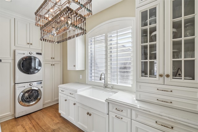 laundry area featuring stacked washer and dryer, a healthy amount of sunlight, light wood-type flooring, a sink, and cabinet space