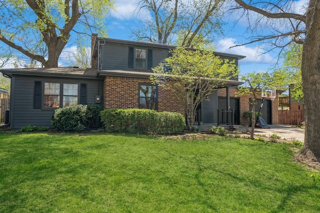 rear view of property featuring fence, a chimney, a yard, and brick siding