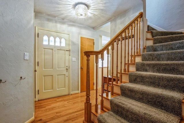 entryway featuring wood finished floors, a textured wall, and stairs