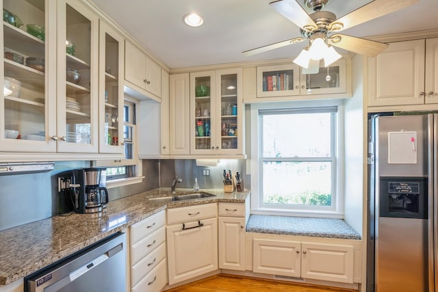kitchen featuring ceiling fan, a sink, light stone counters, glass insert cabinets, and stainless steel appliances