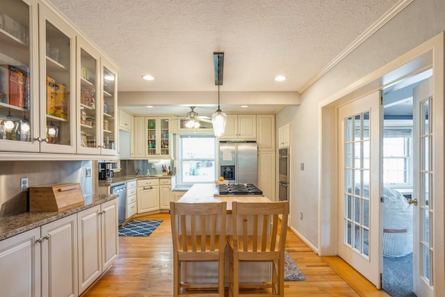 kitchen with stainless steel appliances, a textured ceiling, light stone counters, and light wood-type flooring