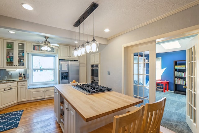kitchen with appliances with stainless steel finishes, a textured ceiling, wood counters, decorative light fixtures, and glass insert cabinets