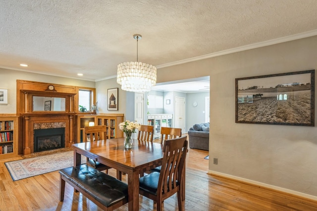 dining room featuring a textured ceiling, a high end fireplace, wood finished floors, baseboards, and a notable chandelier