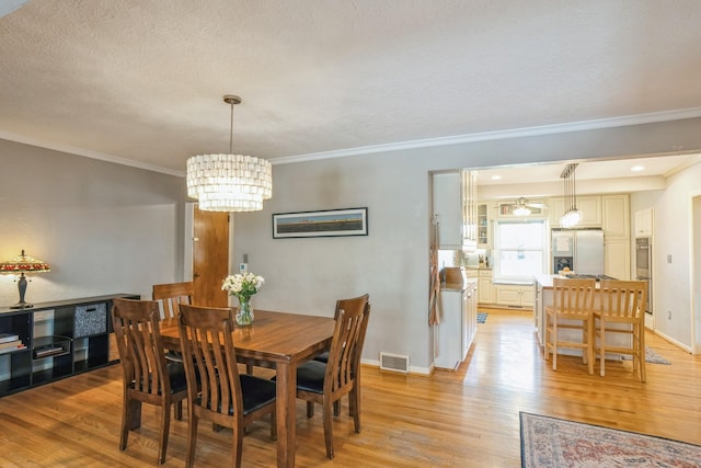 dining space with visible vents, crown molding, an inviting chandelier, baseboards, and light wood-type flooring