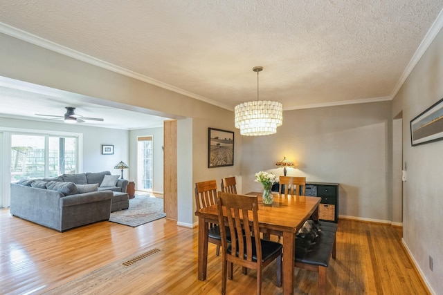 dining area with a textured ceiling, ornamental molding, wood finished floors, and visible vents