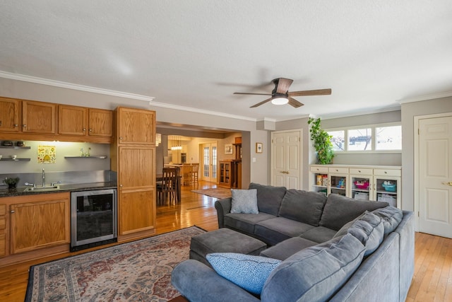 living room featuring a ceiling fan, crown molding, indoor wet bar, wine cooler, and light wood-style flooring