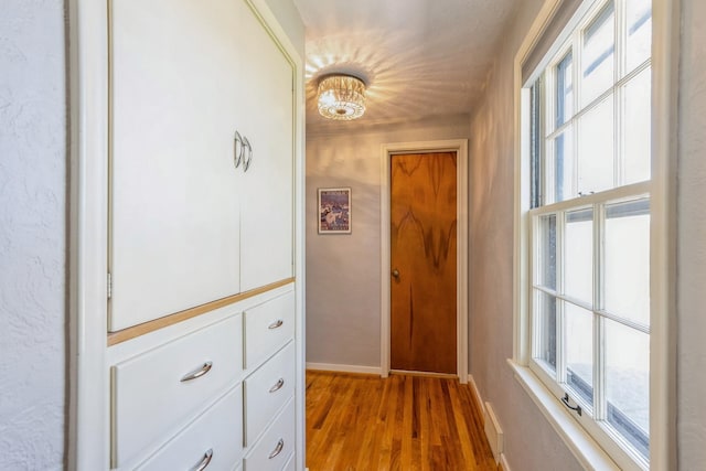 corridor featuring a chandelier, baseboards, visible vents, and wood finished floors