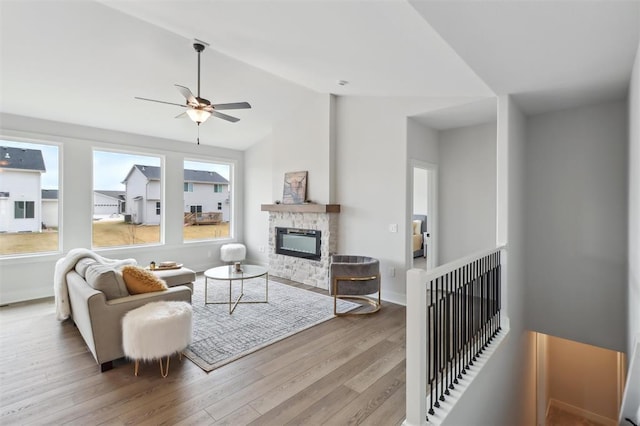 living area with a stone fireplace, a ceiling fan, baseboards, wood finished floors, and lofted ceiling