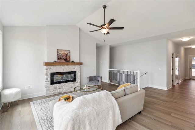living area featuring ceiling fan, a stone fireplace, baseboards, wood finished floors, and lofted ceiling