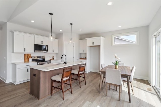 kitchen with a sink, light wood-style flooring, white cabinets, and stainless steel appliances