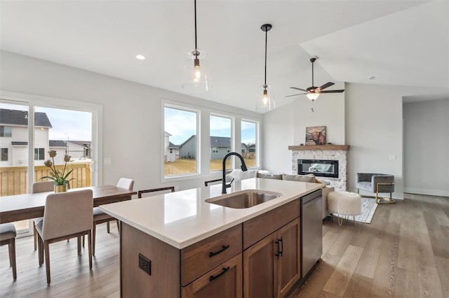 kitchen featuring a sink, light wood-style floors, dishwasher, a stone fireplace, and decorative light fixtures