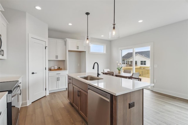 kitchen with appliances with stainless steel finishes, a sink, light countertops, white cabinetry, and light wood-type flooring