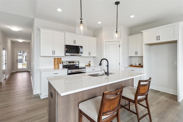 kitchen with a sink, light countertops, white cabinets, light wood-style floors, and stainless steel appliances