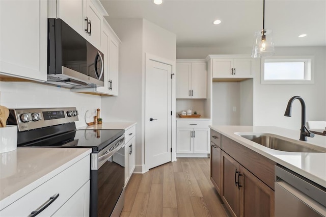 kitchen featuring appliances with stainless steel finishes, hanging light fixtures, a sink, light countertops, and light wood-style flooring