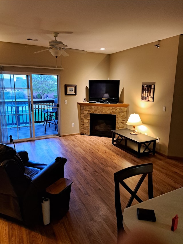 living room featuring baseboards, a stone fireplace, a ceiling fan, and wood finished floors