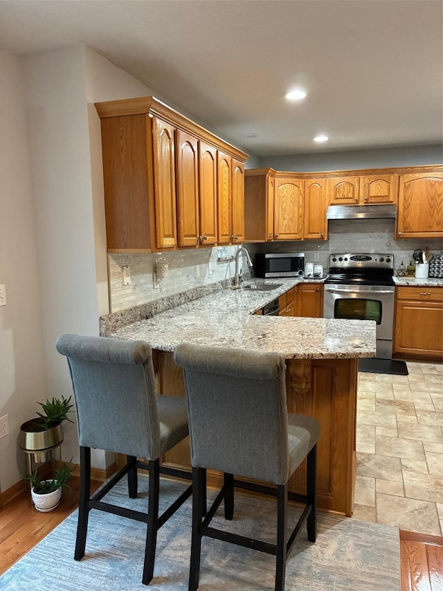 kitchen featuring a breakfast bar area, backsplash, appliances with stainless steel finishes, a sink, and a peninsula