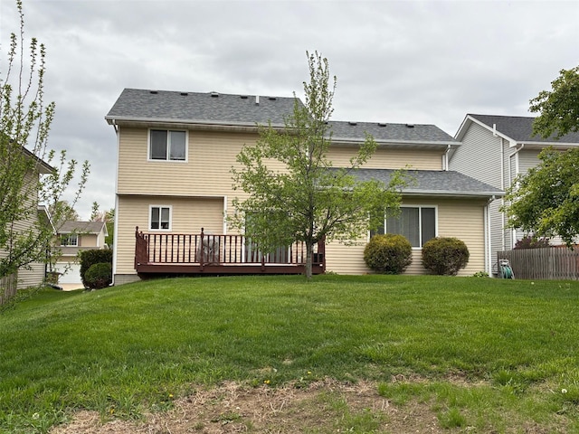 rear view of property with a yard, a deck, and roof with shingles