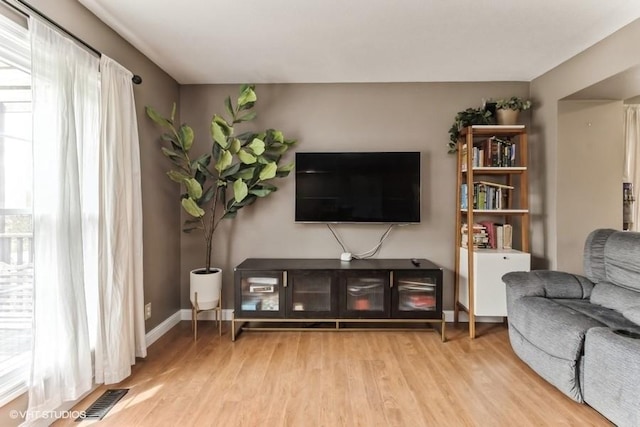 living room featuring visible vents, light wood finished floors, baseboards, and a healthy amount of sunlight