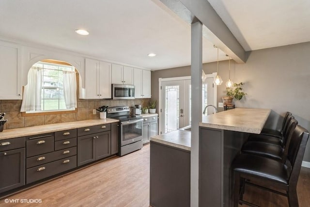 kitchen with appliances with stainless steel finishes, a kitchen breakfast bar, white cabinetry, a peninsula, and decorative backsplash