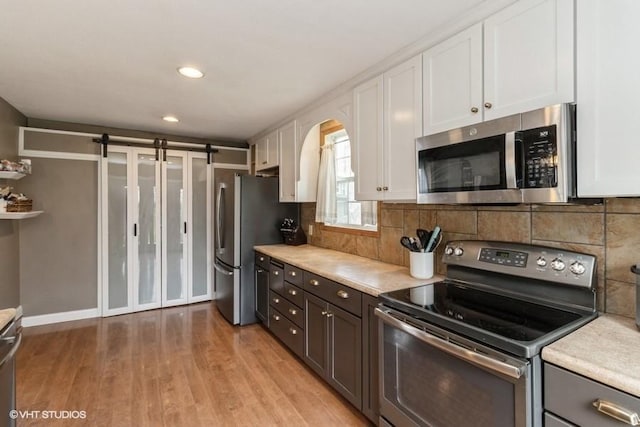 kitchen featuring appliances with stainless steel finishes, light wood-style floors, light countertops, white cabinetry, and tasteful backsplash