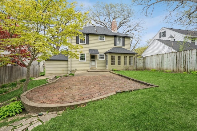 back of house featuring a yard, a patio, a shingled roof, and a chimney
