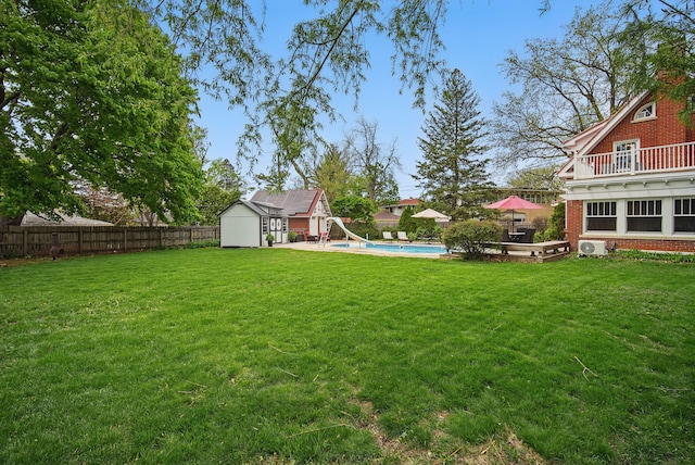view of yard featuring an outbuilding, a fenced in pool, a balcony, a fenced backyard, and a storage unit