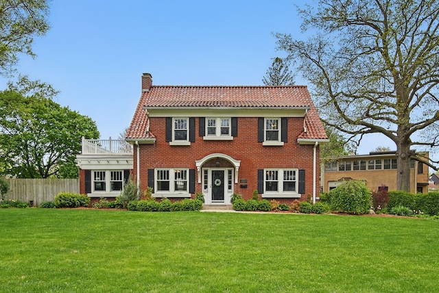 colonial house featuring fence, a chimney, a tile roof, and a front yard