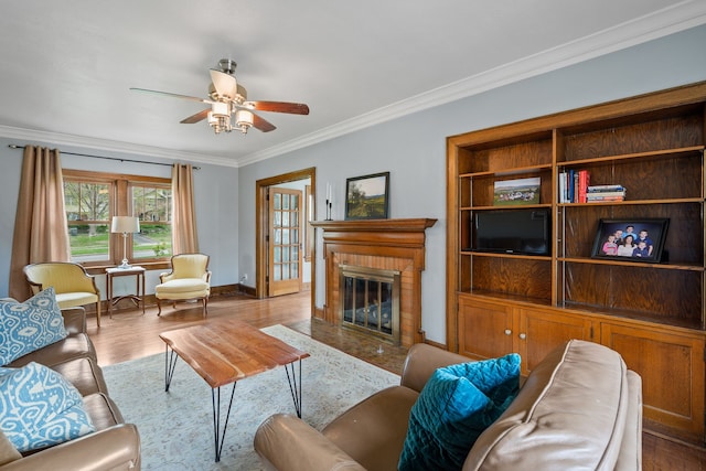 living area featuring crown molding, a brick fireplace, ceiling fan, and wood finished floors