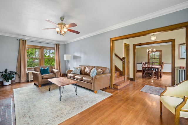 living room featuring light wood-style floors, ceiling fan with notable chandelier, baseboards, ornamental molding, and stairway