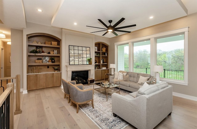 living room featuring light wood-style floors, baseboards, a glass covered fireplace, and ceiling fan